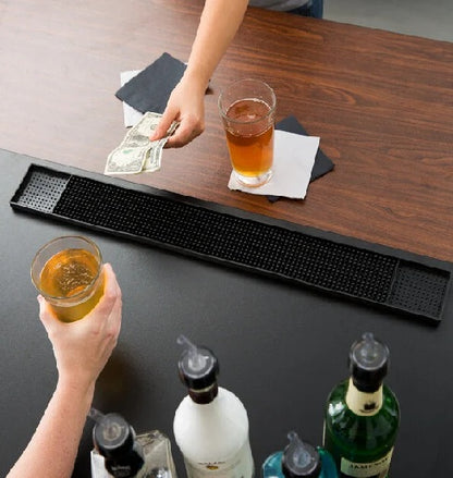 Two people holding glasses of beer over a bar tray with bottles on a wooden surface.